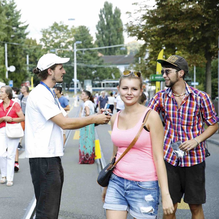 Ein Bild welches einen jungen Mann zeigt, der auf der Strasse bei Passanten für eine Kampagne wirbt